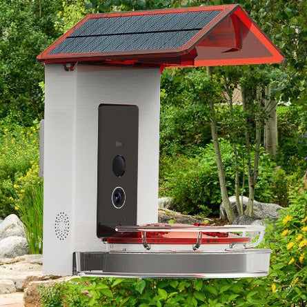 A solar powered hummingbird feeder with a red roof against a blurry garden background